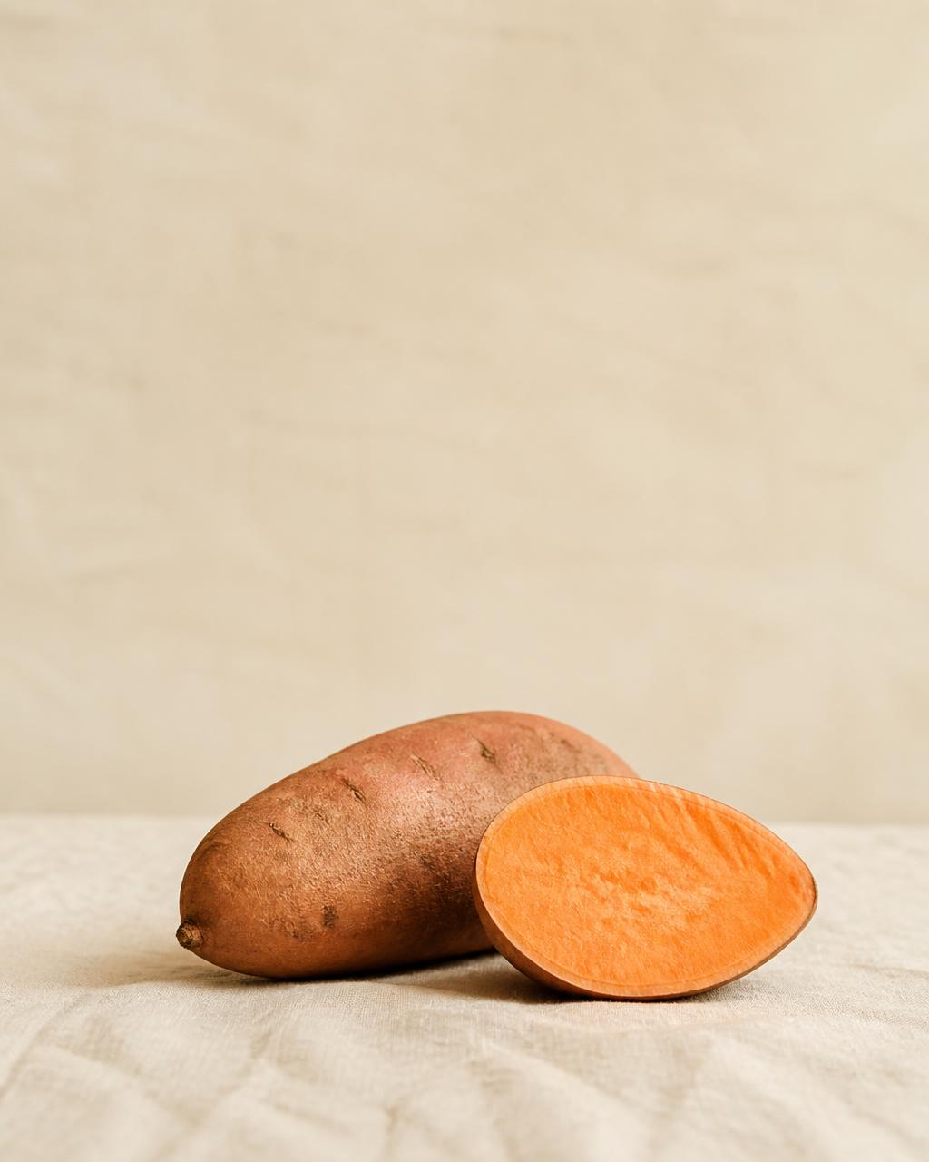 A whole sweet potato with a cut half showing orange flesh