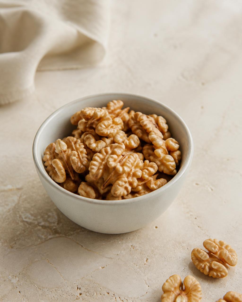 Shelled walnut halves in a small pale ceramic bowl on a warm cream stone surface