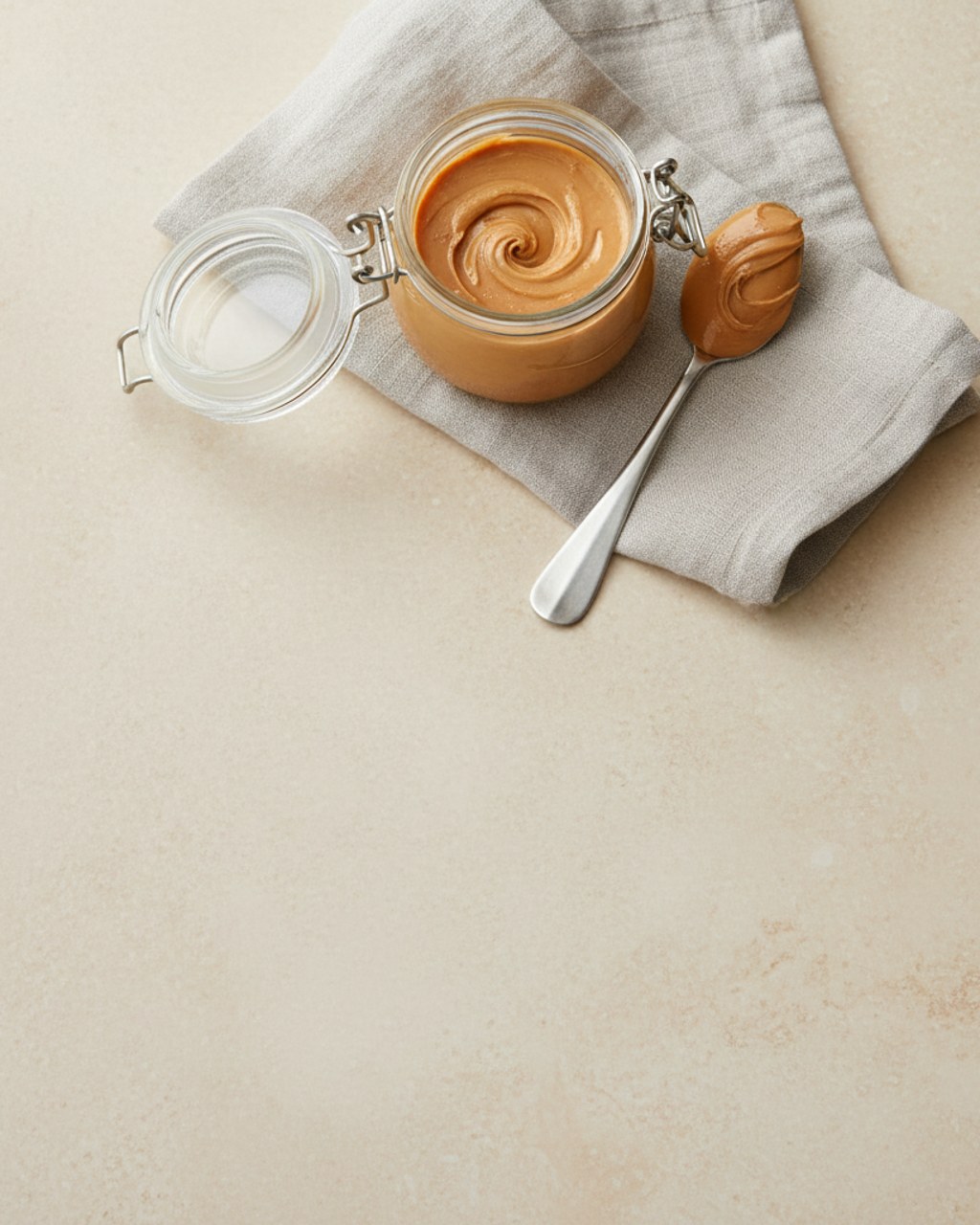 An open jar of pure peanut butter with a spoonful beside it