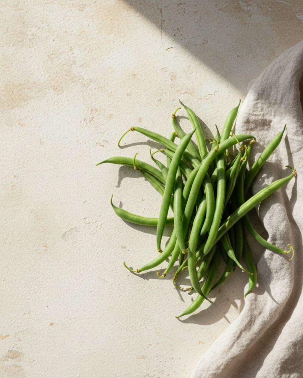 A loose bundle of fresh green beans resting on warm cream linen